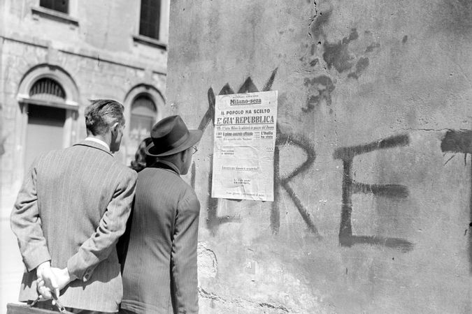 Passanti leggono il titolo della seconda edizione del quotidiano Milano-Sera affisso a un muro